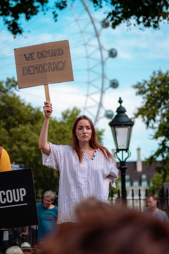 Eine demonstrierende Frau hält ein Schild mit der Aufschrift "We demand democracy" hoch.