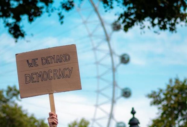 Eine demonstrierende Frau hält ein Schild mit der Aufschrift "We demand democracy" hoch.